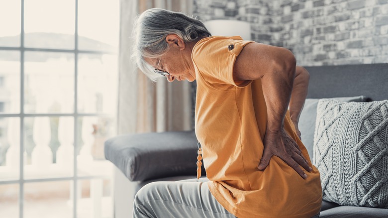 older woman on sofa grabbing back in pain