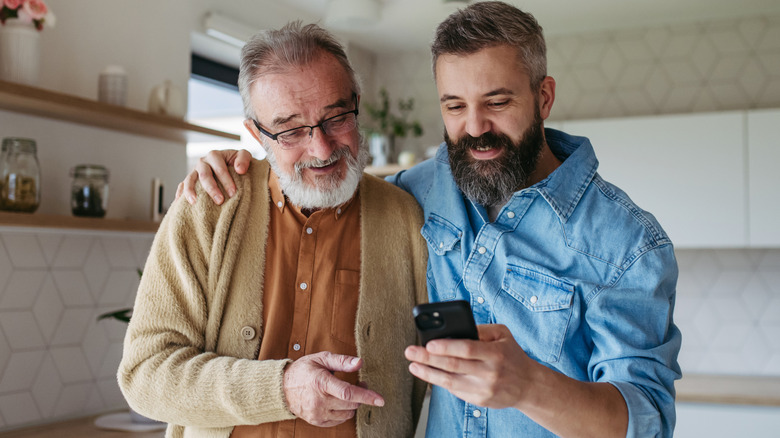 A son showing his father pictures on his smartphone