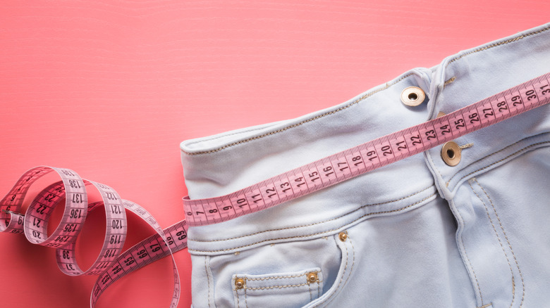 A pink measuring tape around summer jeans with an all pink background 