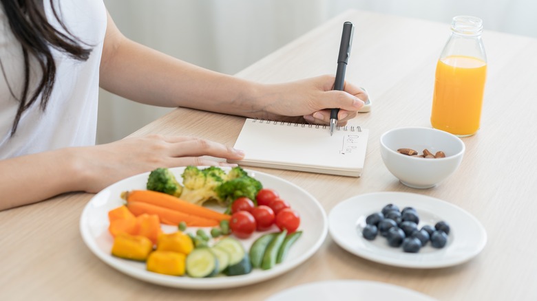 woman's hand recording her food intake in a diary