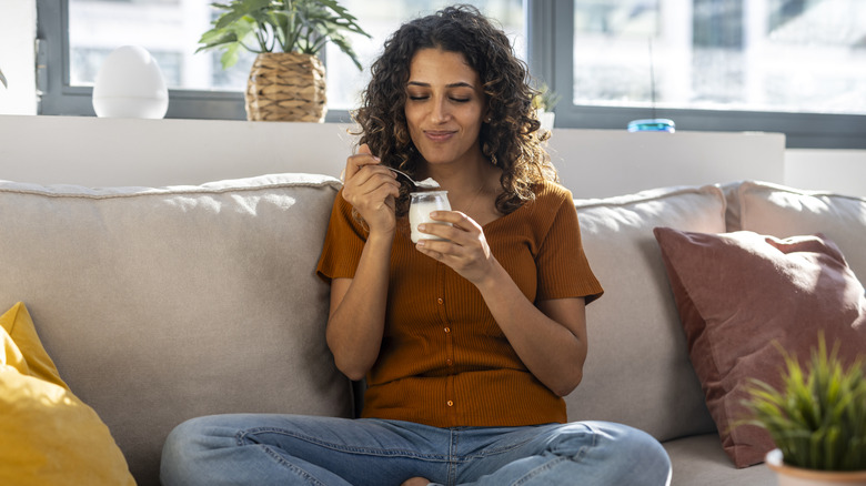 A woman eating yogurt while sitting on her couch