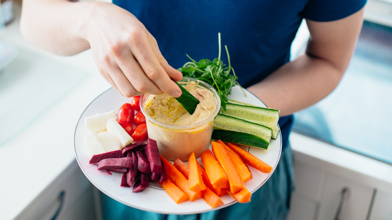 man's hands dipping vegetables into hummus