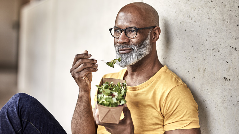 Smiling man eating salad outdoors