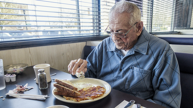 Man sprinkling salt on breakfast plate