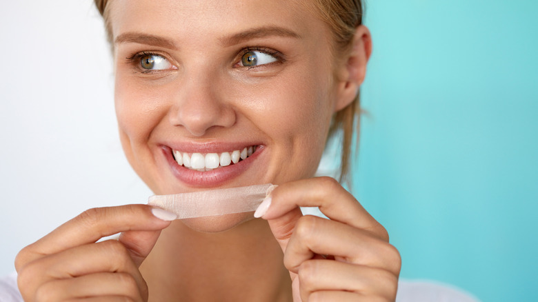 A woman applies a whitening strip to her teeth