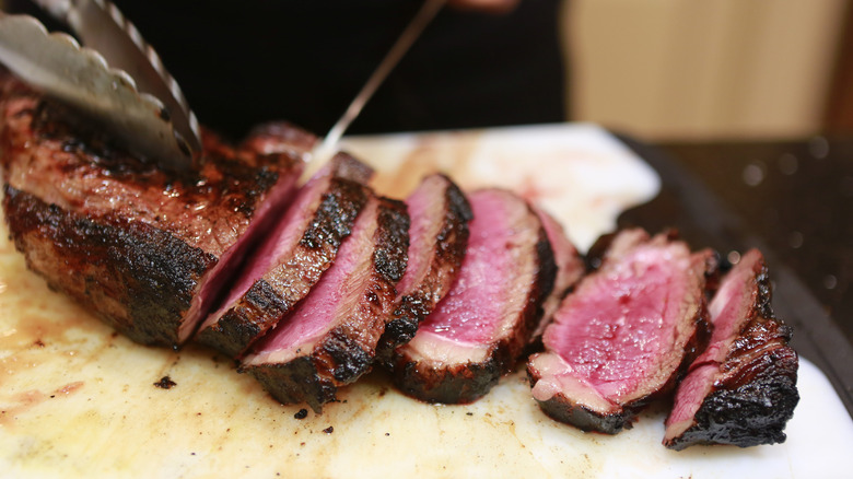 A knife slicing through a large cut of beef