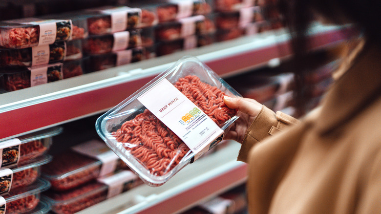 A package of ground beef from a point of view over a woman's shoulder