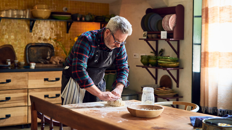 senior man making bread dough in kitchen