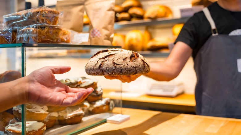 bakery worker hands rustic bread loaf to customer