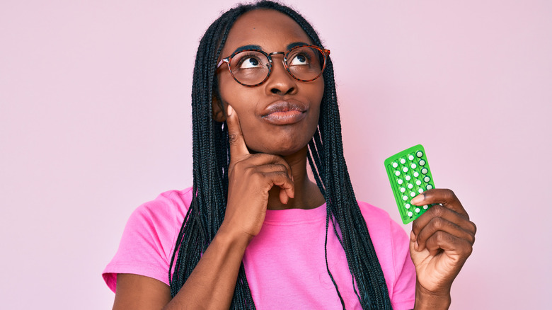 Woman holding pills wondering