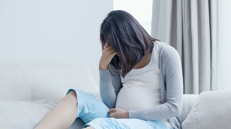 Pregnant woman on bed hanging head