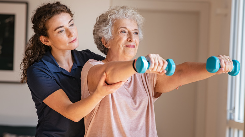 a young physical therapist helps an older woman with shoulder strengthening 