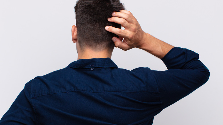 man with back turned scratching head