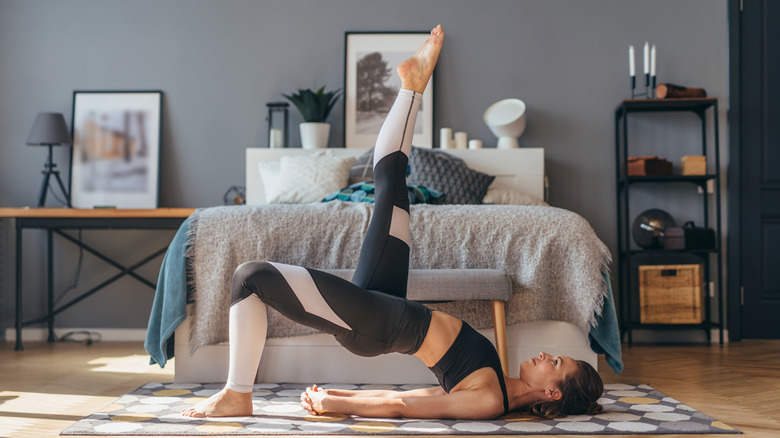 A woman in workout clothes doing a hip bridge variation in her room