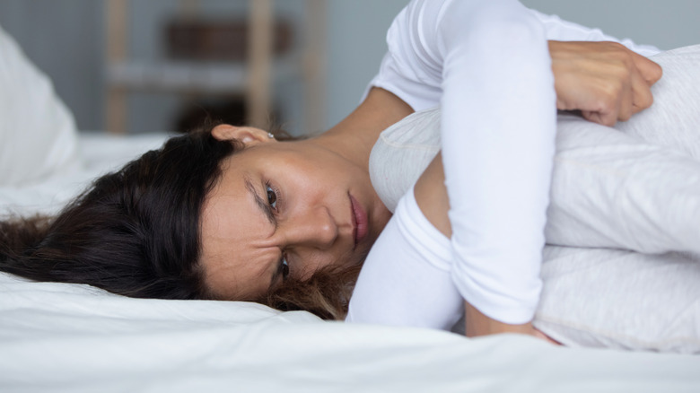 an anxious looking woman lies in fetal position 