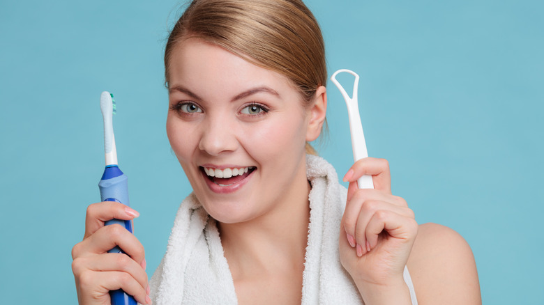 woman holding toothbrush and tongue scraper