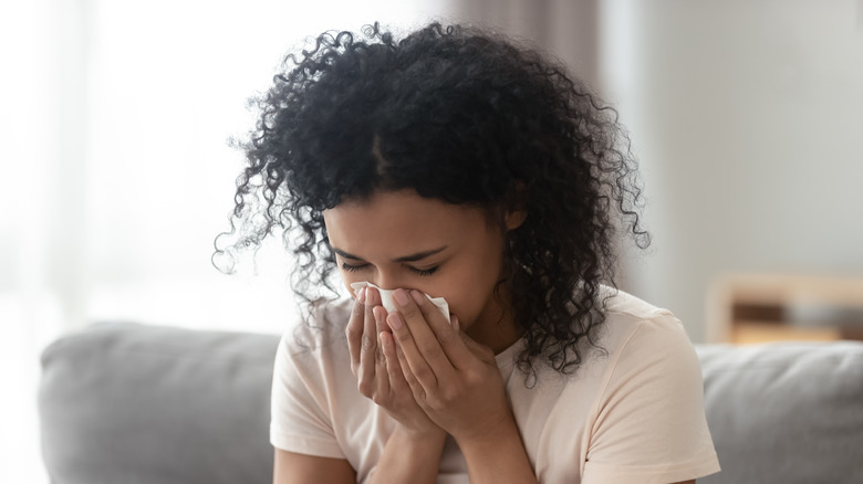 A woman sneezing while on her couch