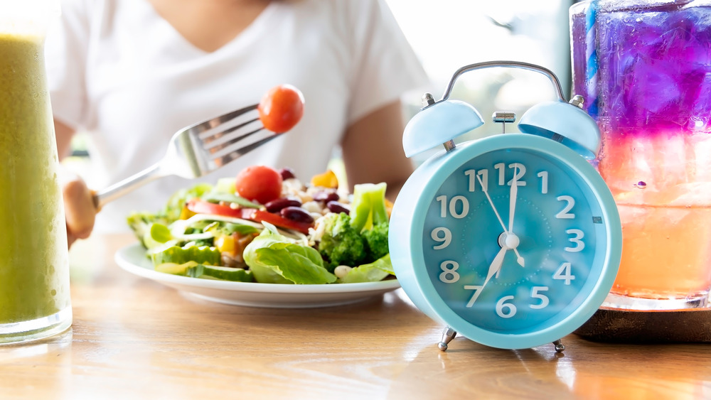 person eating a salad with a clock on the table