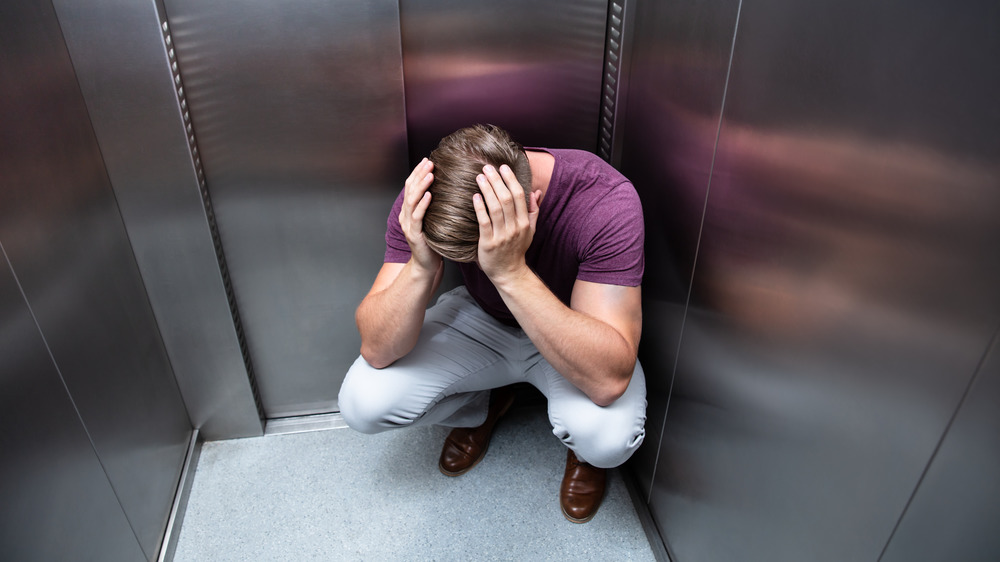 Man crouched in elevator with hands on head