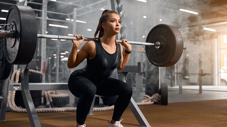 young woman performing squats with heavy barbell