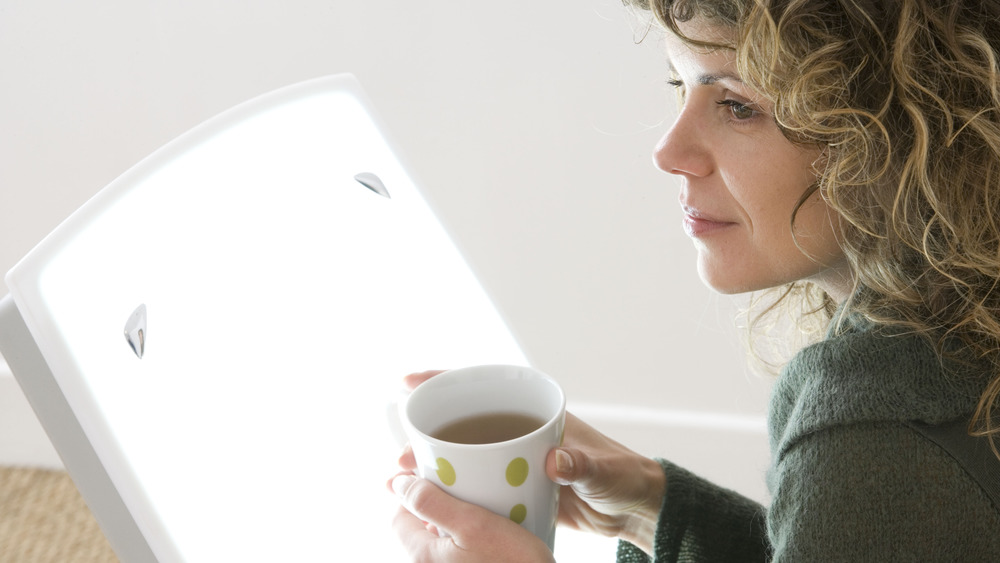 Woman in front of light therapy box holding cup of coffee