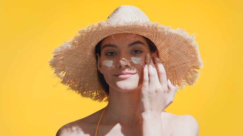 woman in sunhat applies sunscreen