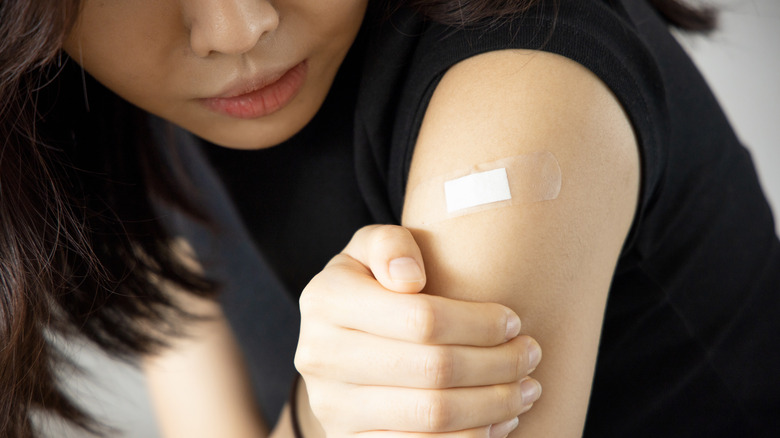 Close up of woman examining bandage from vaccination shot on shoulder