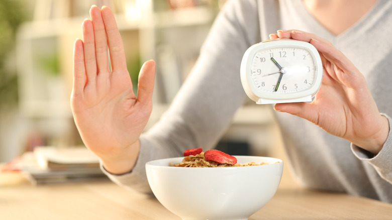 woman holding her hand over her food next to a clock