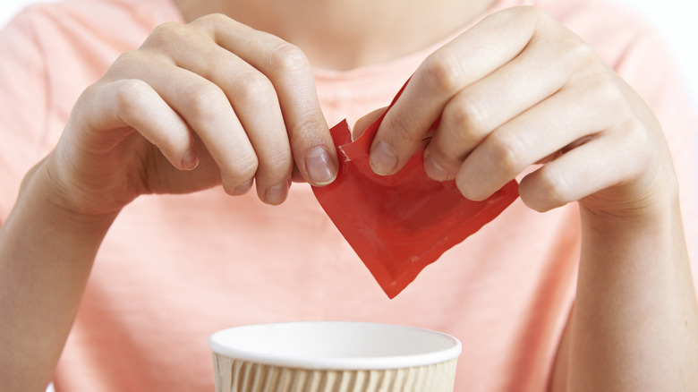 hands opening sweetener packet over coffee