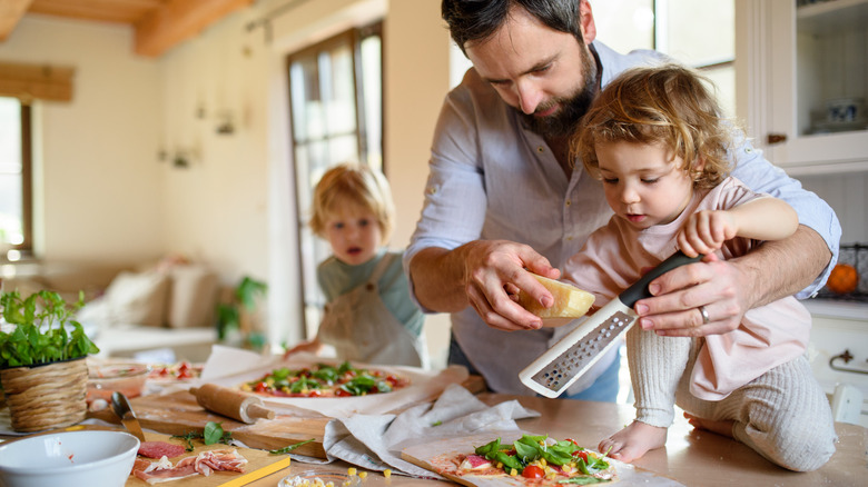 man grating cheese in kitchen with little children