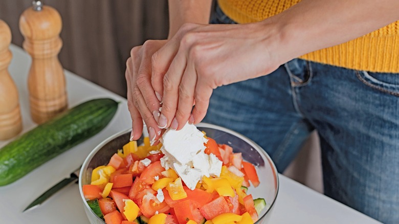 woman putting feta cheese on a salad