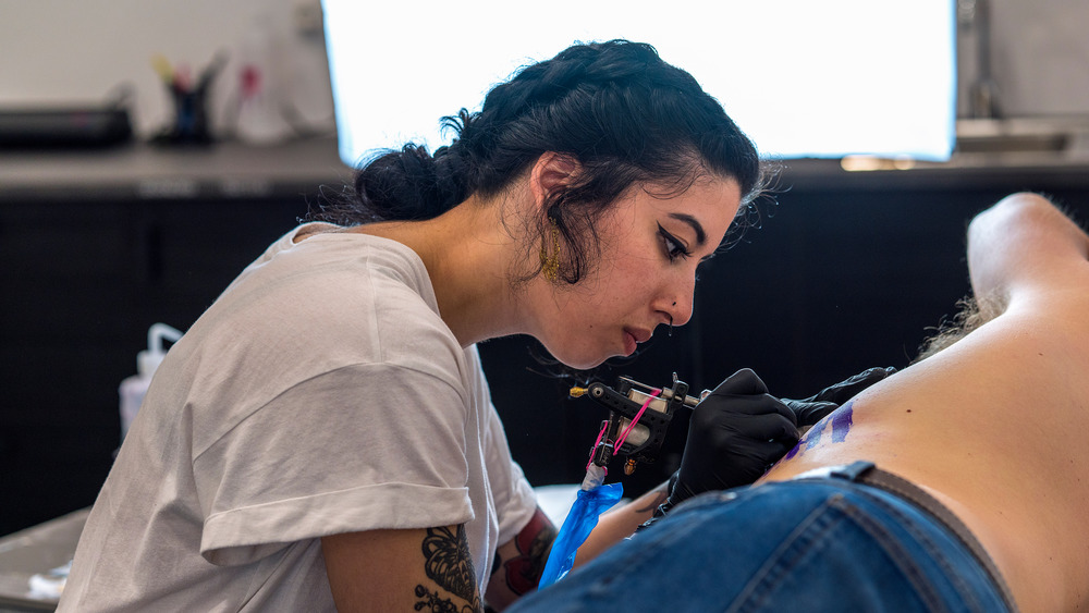 female tattoo artist tattooing on a clients ribcage 