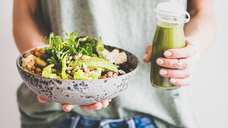 Close up of a woman holding a bowl of vegetables and a green smoothie