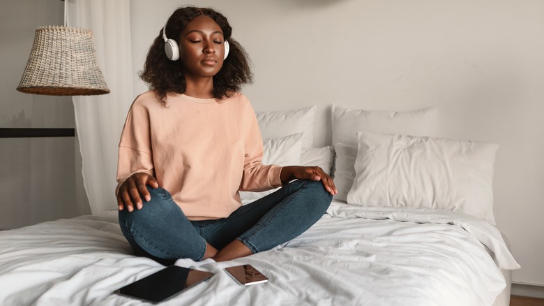 Woman meditating while sitting on bed with headphones on