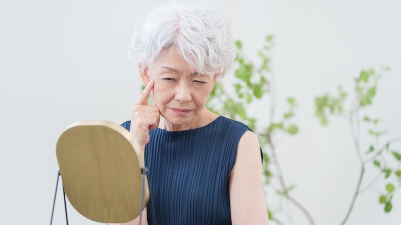 older woman looking in mirror at face