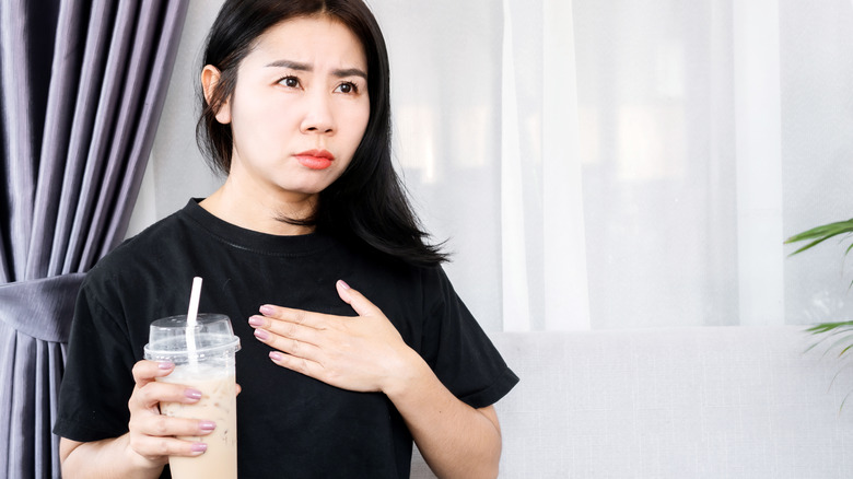 woman having heart palpitations while holding large coffee