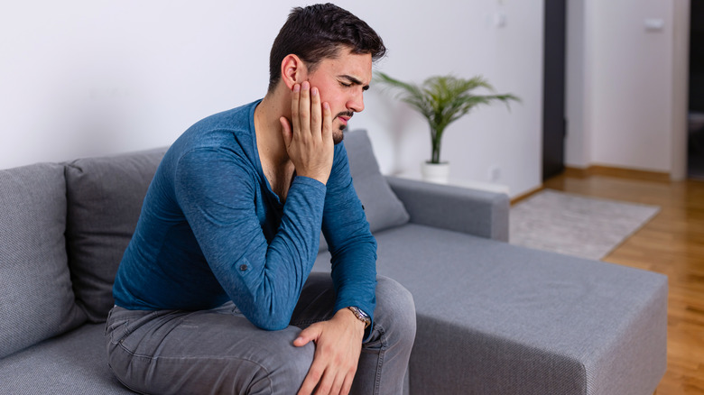 man with toothache sitting on couch