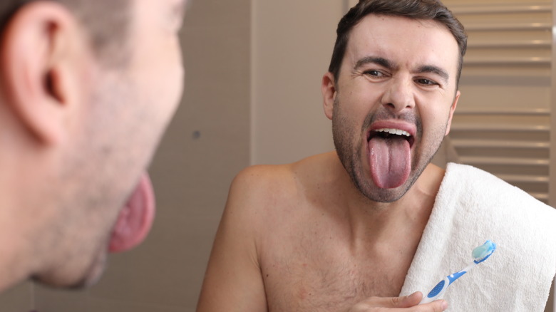 man sticking out tongue while holding toothbrush