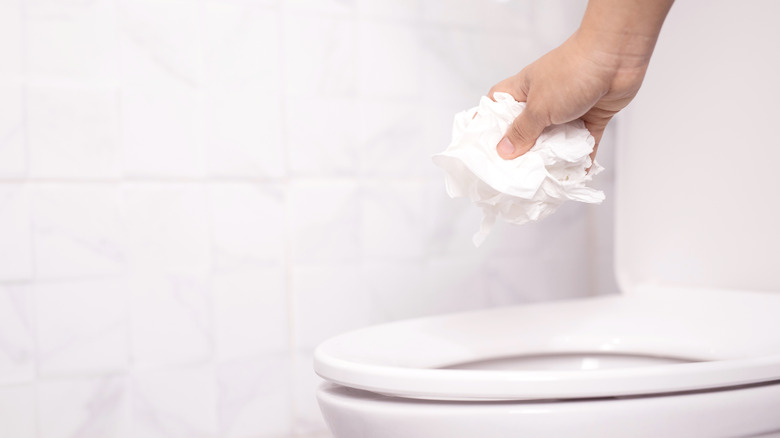 Hand throwing tissue in toilet