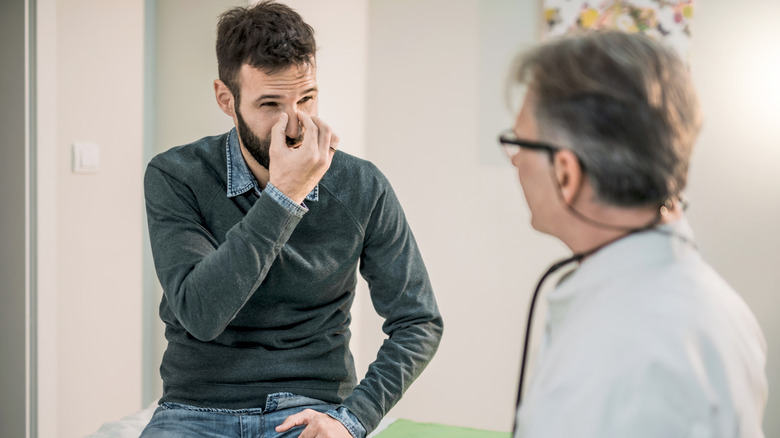 patient touching his nose describing trouble breathing to doctor