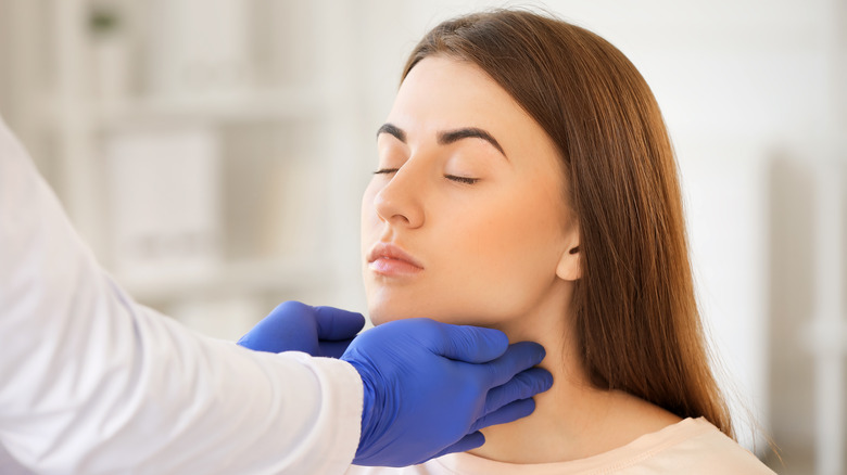 doctor checking woman's thyroid