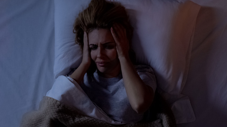 Woman holding head in bed