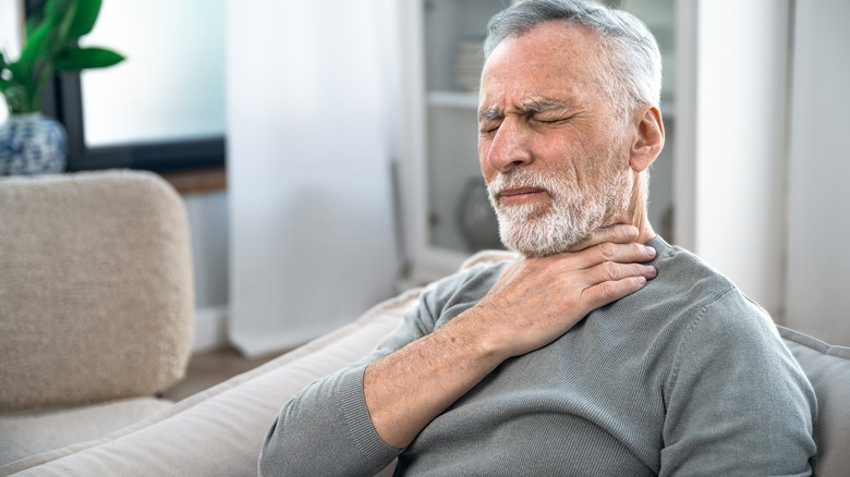 Older man in discomfort holds throat