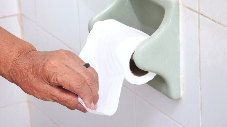 woman's hand reaching for a roll of toilet paper