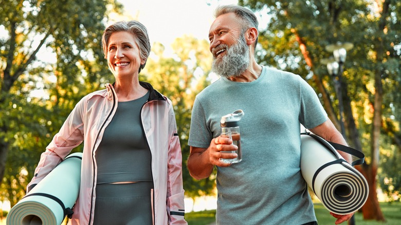 senior couple smiling and walking with yoga mats