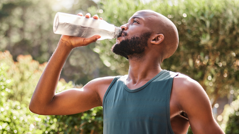 man drinking water while holding a yoga mat