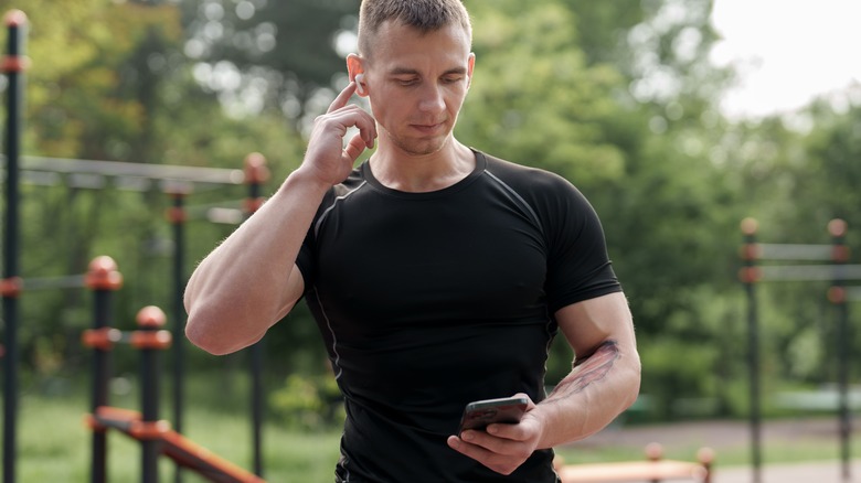 Man wearing fitness gear, wearing headphones and holding phone