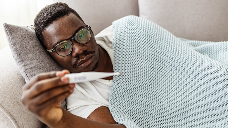 Sick man holding thermometer