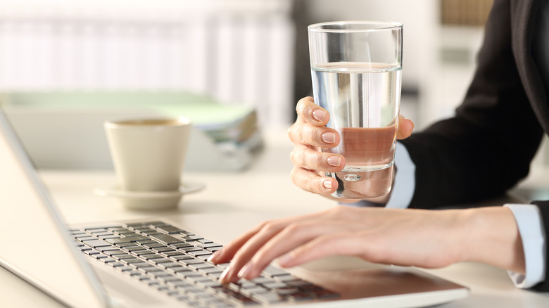 Hands typing on laptop and holding water glass
