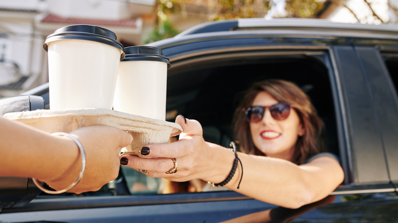 Woman being handed two coffees in drive-thru